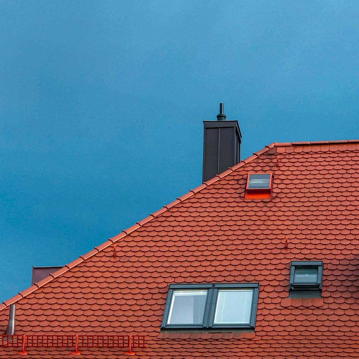 Rotes Ziegeldach mit Dachfenstern und Schornstein vor blauem Himmel