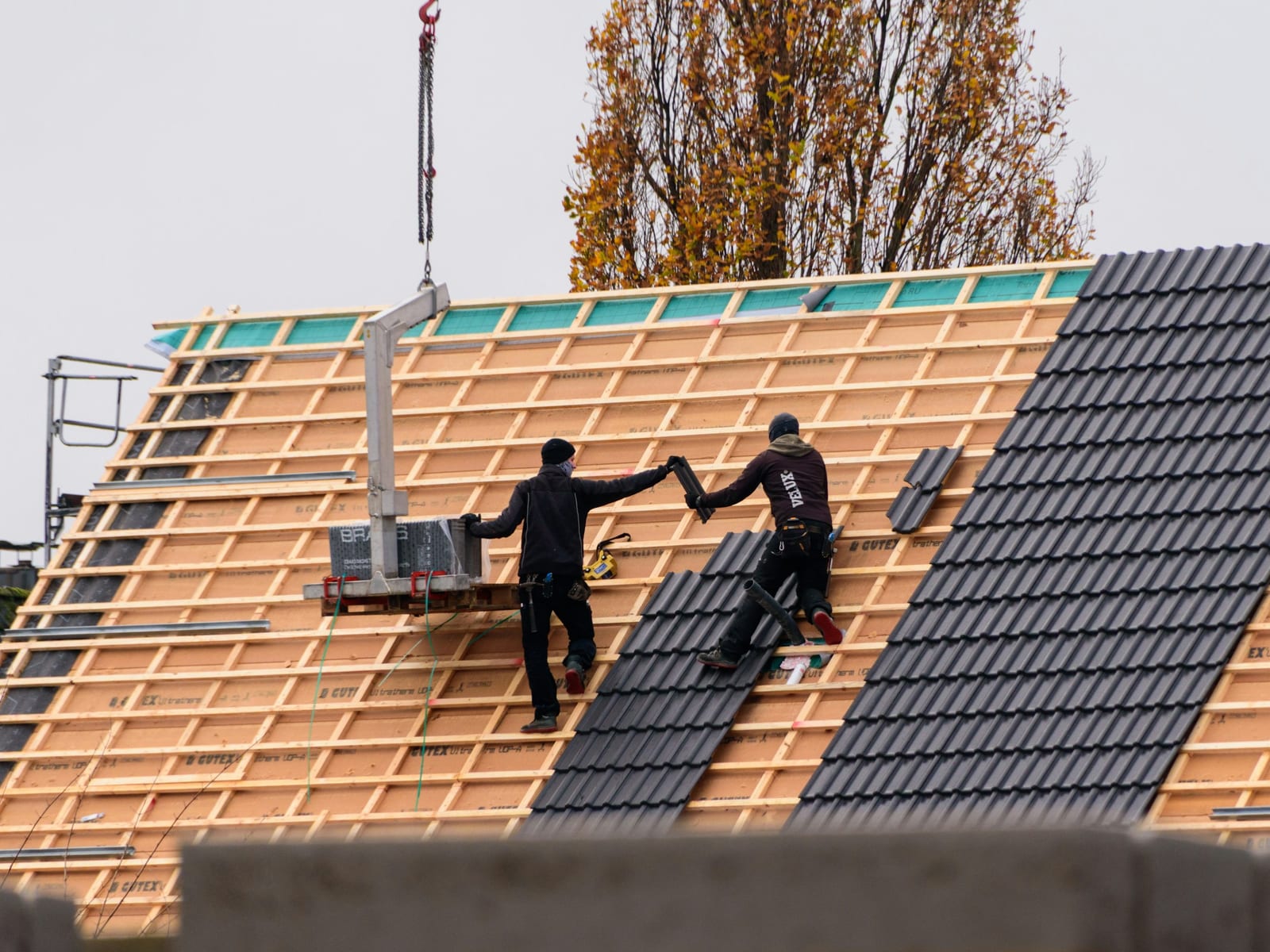 Zwei Dachdecker verlegen dunkle Dachziegel auf einem neuen Steildach